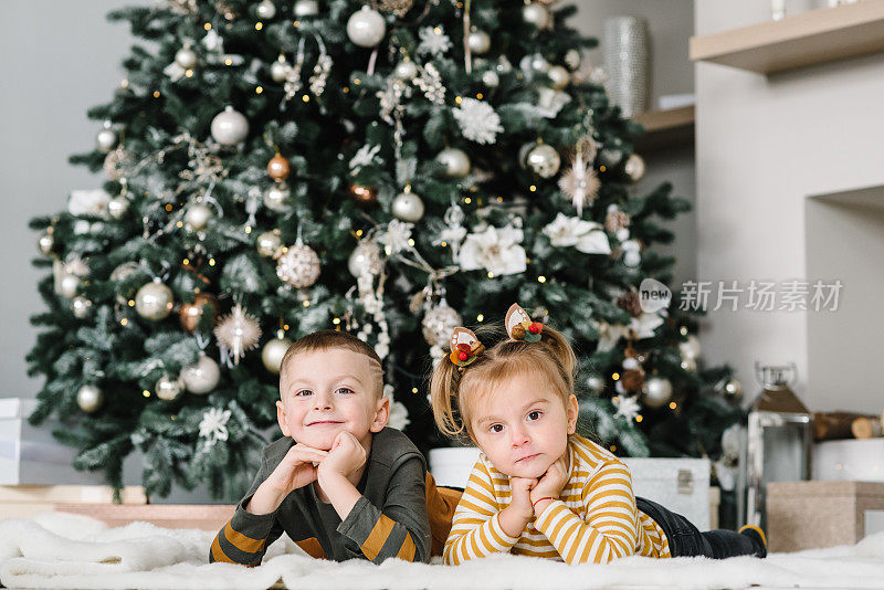 Childs playing near Christmas tree. Happy children hugging at a home. Brother and sister. Happy New Year and Merry Christmas. Ð¡oncept of a family holiday. Decorated interior room of a house. Closeup.